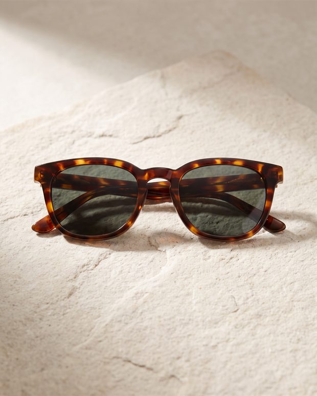 Gafas de sol con montura de acetato sobre una superficie de piedra clara, fotografía de producto generada con IA